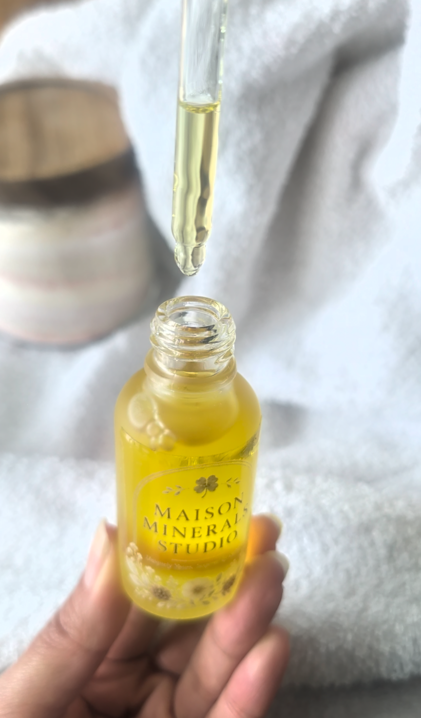Carrier oil being poured in a slow thread over a dry mineral blend, catching the light